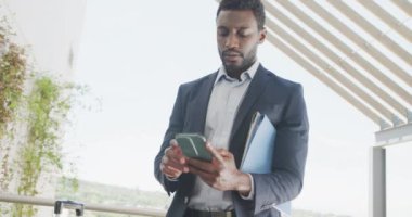 Mutlu Afro-Amerikan iş adamı akıllı telefon kullanıyor ve ofiste kutlama yapıyor, ağır çekimde. Modern ofis, iş ve finans sektöründe çalışmak.