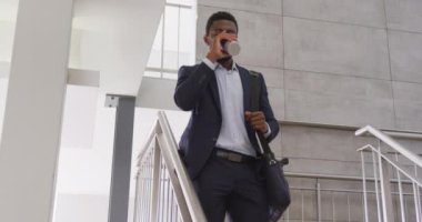 Mutlu Afro-Amerikan iş adamı merdivenlerden inip ofiste kahve içiyor, ağır çekimde. Modern ofis, iş ve finans sektöründe çalışmak.