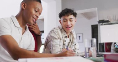 Three happy diverse male teenage friends writing and talking at home, slow motion. Spending quality time at home together.