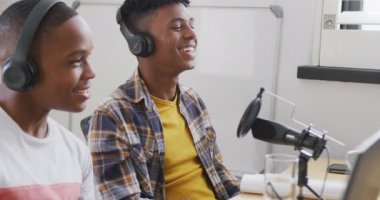 Happy african american male teenage friends using laptop and recording podcast, slow motion. Spending quality time at home together.