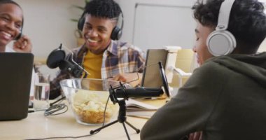 Happy diverse male teenage friends using laptop and recording podcast, slow motion. Spending quality time at home together.