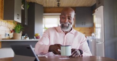 Happy senior african american man in log cabin, using tablet for online shopping, slow motion. Free time, domestic life and communication concept.