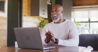 Happy senior african american man in log cabin, using laptop for video call, slow motion. Free time, domestic life and communication concept.