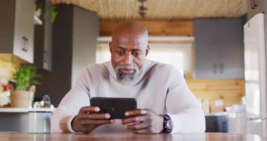 Happy senior african american man in log cabin, using smartphone for video call, slow motion. Free time, domestic life and communication concept.