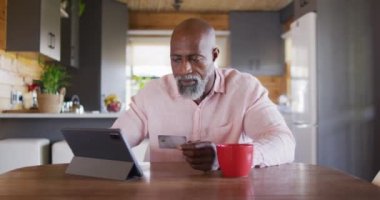 Happy senior african american man in log cabin, using tablet for online shopping, slow motion. Free time, domestic life and communication concept.