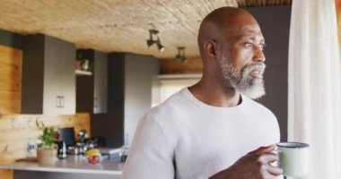 Senior african american man spending time in log cabin and drinking coffee, slow motion. Free time, domestic life and leisure concept.