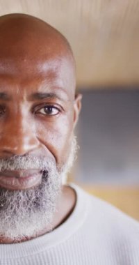 Vertical video of portrait of happy senior african american man spending time in log cabin. Free time, domestic life and nature concept.