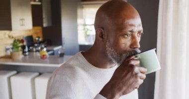 Senior african american man spending time in log cabin and drinking coffee, slow motion. Free time, domestic life and leisure concept.