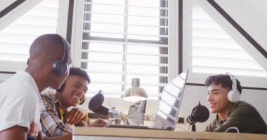 Happy diverse male teenage friends using laptop and recording podcast, slow motion. Spending quality time at home together.