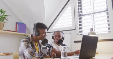 Happy african american male teenage friends using laptop and recording podcast, slow motion. Spending quality time at home together.
