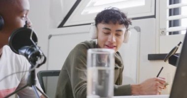Happy diverse male teenage friends using laptop and recording podcast, slow motion. Spending quality time at home together.
