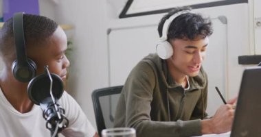 Happy diverse male teenage friends using laptop and recording podcast, slow motion. Spending quality time at home together.
