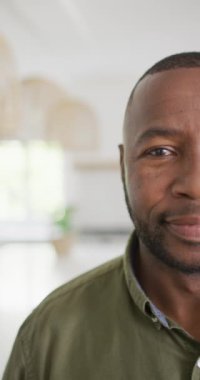 Vertical video of portrait of happy african american man looking at camera and smiling. Spending quality time at home.