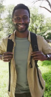 Vertical video of portrait of happy african american man in park, slow motion. Nature, hiking and park concept.
