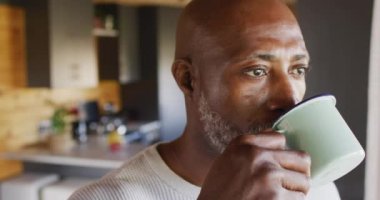 Senior african american man spending time in log cabin and drinking coffee, slow motion. Free time, domestic life and leisure concept.