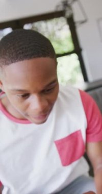 Vertical video of happy diverse male teenage friends using smartphone. Spending quality time at home together.
