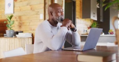 Happy senior african american man in log cabin, using laptop for video call, slow motion. Free time, domestic life and communication concept.