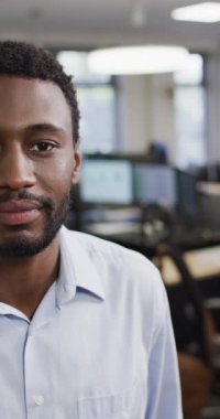 Afro-Amerikan iş adamının kameraya bakıp ofiste gülümsemesinin dikey videosu. Modern ofis, iş ve finans sektöründe çalışmak.