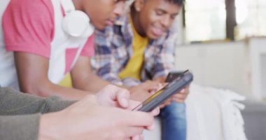 Video of happy diverse male teenage friends using smartphones, slow motion. Spending quality time at home together.