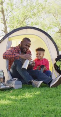 Vertical video of african american man and his son sitting in tent in garden. Spending quality time at home.
