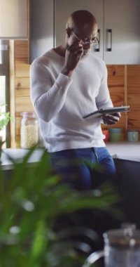 Vertical video of senior african american man spending time in log cabin using tablet. Free time, domestic life and nature concept.