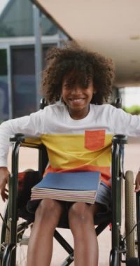 Tekerlekli sandalyedeki gülümseyen Afrikalı Amerikalı okul çocuğunun dikey video portresi. Koridorda, kopyalama alanında. Eğitim, çocukluk, kapsayıcılık, okul ve öğrenim kavramı.