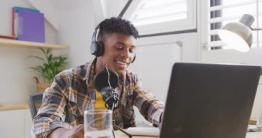 Happy african american male teenage boy using laptop and recording podcast, slow motion. Spending quality time at home.