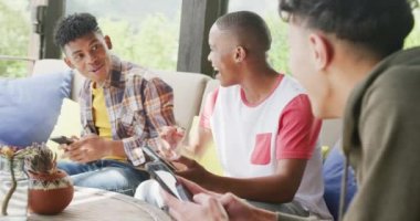 Video of happy diverse male teenage friends using smartphones, slow motion. Spending quality time at home together.