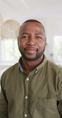 Vertical video of portrait of happy african american man looking at camera and smiling. Spending quality time at home.