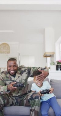 Vertical video of african american male soldier and his son playing video games. Spending quality time at home.