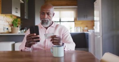 Happy senior african american man in log cabin, using smartphone for online shopping, slow motion. Free time, domestic life and communication concept.