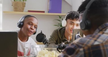 Happy diverse male teenage friends using laptop and recording podcast, slow motion. Spending quality time at home together.
