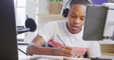 Happy african american male teenage boy recording podcast using laptop, slow motion. Spending quality time at home.