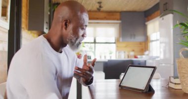 Mutlu kıdemli Afro-Amerikan adam masada oturup fotokopi alanı olan tablet kullanıyor, yavaş çekim. Boş zaman, ev hayatı ve iletişim konsepti.