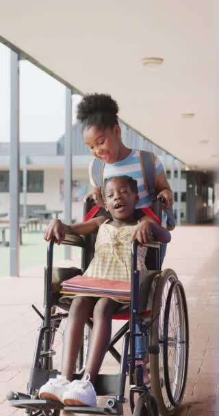 两个快乐 多样化的女学生坐在轮椅上推着另一个的垂直视频复制了空间 包容性 学校和学习概念 — 图库视频影像