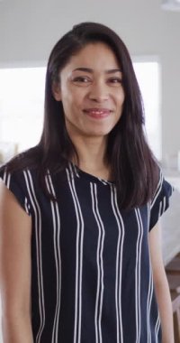 Vertical video portrait of happy biracial woman at home smiling to camera, in slow motion. Free time, happiness and lifestyle concept.