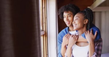 Mutlu Afro-Amerikan çifti pencereden bakıp odunluk kulübesinde kucaklaşıyorlar, ağır çekimde. Yaşam tarzı, ev hayatı, kırsal ve doğa kavramı.