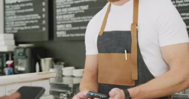 Diverse male barista and female customer paying with smartphone in cafe. Local business owner and hospitality concept.