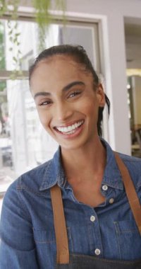 Vertical video of portrait of happy biracial female barista in her cafe shop. Cafe, barista and business concept.