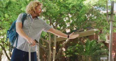 Happy diverse couple hailing taxi with luggage and takeaway coffee in city street. City break, travel and hospitality concept.