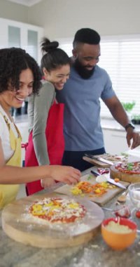 Farklı erkek ve kadın arkadaşlarının mutfakta yavaş çekimde pizza yaptıklarını gösteren dikey bir video. Arkadaşlık, yemek pişirme ve yaşam tarzı konsepti.