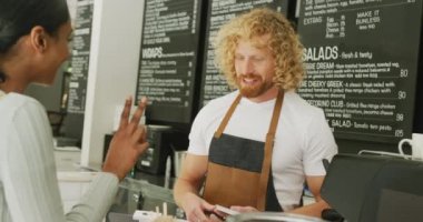 Happy diverse woman ordering coffee and talking with male barista in cafe. Local business owner and hospitality concept.