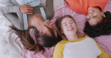 Happy diverse teenager girls friends laughing and lying on bed, slow motion. Friends, leisure, spending quality time at home concept.