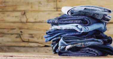 Close up of folded jeans with different shades on wooden background with copy space. Denim day, material, style and design concept.