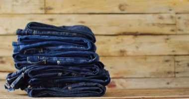 Close up of folded jeans with different shades on wooden background with copy space. Denim day, material, style and design concept.