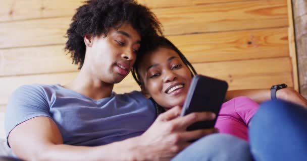 Happy African American Couple Using Smartphone Sitting Sofa Log Cabin — стокове відео