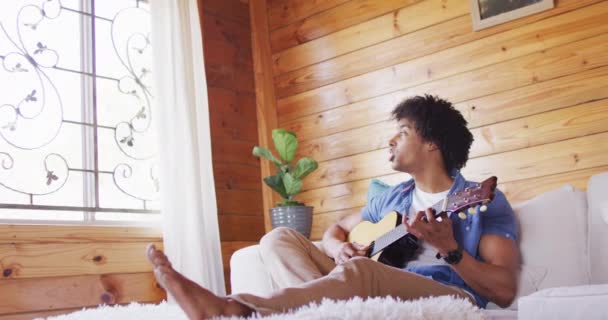 Happy African American Man Sitting Sofa Playing Guitar Log Cabin — Αρχείο Βίντεο