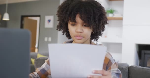 African American Teenage Girl Reading Paperwork Using Laptop Home Slow — Stockvideo