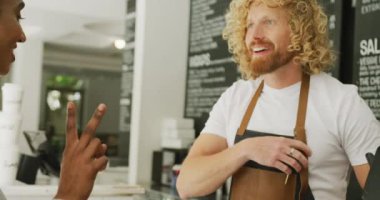 Happy diverse woman buying coffee and talking with male barista in cafe. Local business owner and hospitality concept.