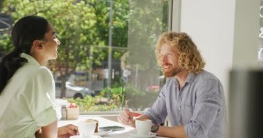 Happy diverse couple drinking coffee and talking at a table in cafe. City break, travel, local business and hospitality concept.